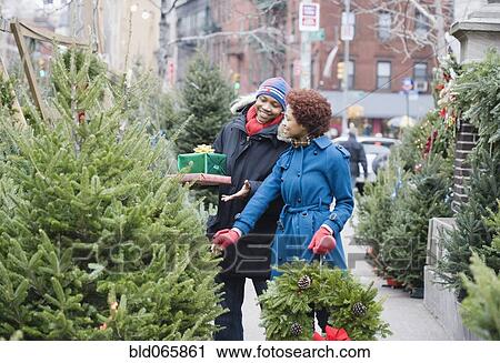 Stock Image - African man choosing Christmas tree with girlfriend. Fotosearch