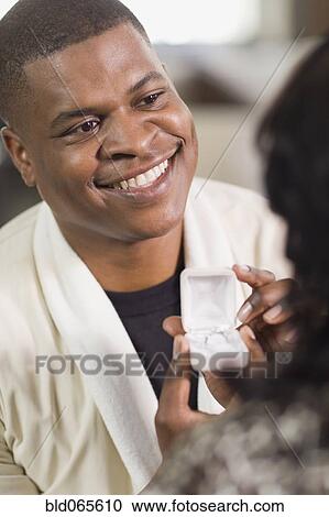 Stock Image - African man giving girlfriend engagement ring. Fotosearch