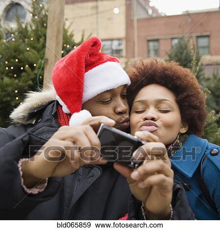 Stock Photo - African man in santa hat taking self-portrait with girlfriend. Fotosearch