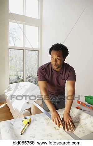 Stock Photo - African man measuring wallpaper. Fotosearch