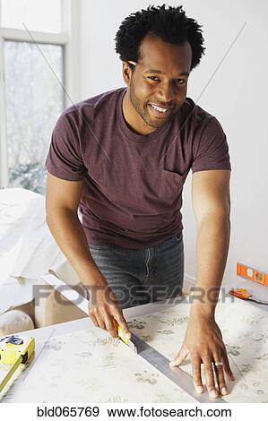 Stock Photo - African man measuring wallpaper. Fotosearch