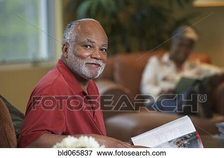 Stock Photo - African man reading magazine in livingroom. Fotosearch