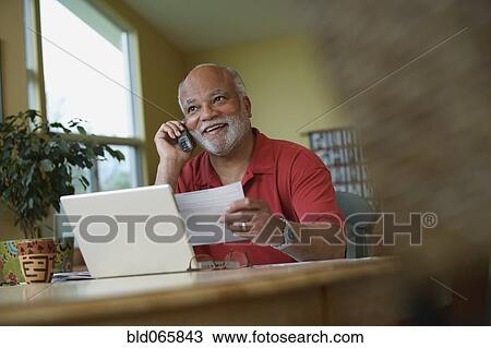 Stock Image - African man talking on telephone while paying bills. Fotosearch
