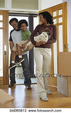 Stock Image - African mother and father carrying carpet and son into new home. Fotosearch
