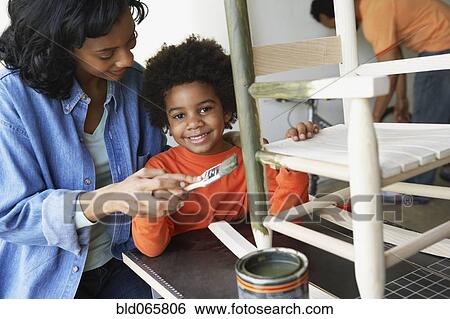 Stock Photograph - African mother and son painting rocking chair. Fotosearch