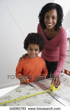 Stock Image - African mother teaching son to measure wallpaper. Fotosearch