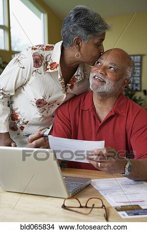 Picture - African woman kissing husband as he pays bills. Fotosearch