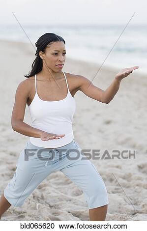 Stock Image - African woman practicing yoga at beach. Fotosearch