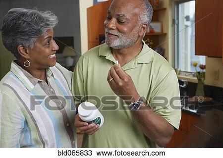 Stock Image - African woman watching husband take vitamin. Fotosearch