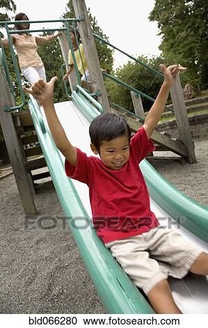 Stock Image - Asian boy sliding down slide on playground. Fotosearch