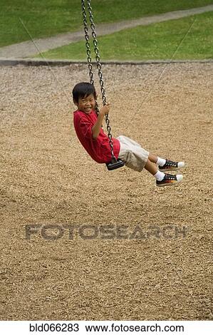 Stock Image - Asian boy swinging on playground. Fotosearch