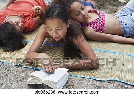 Stock Photograph - Asian girl laying and reading with friends. Fotosearch