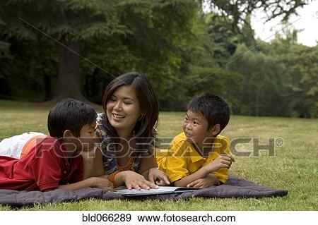Asian mother reading book to sons in park View Large Photo Image Stock Photo - Asian mother reading book to sons in park. Fotosearch