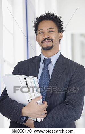 Stock Image - Confident African businessman holding paperwork. Fotosearch