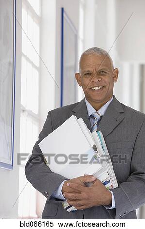 Stock Photography - Confident African businessman holding paperwork. Fotosearch