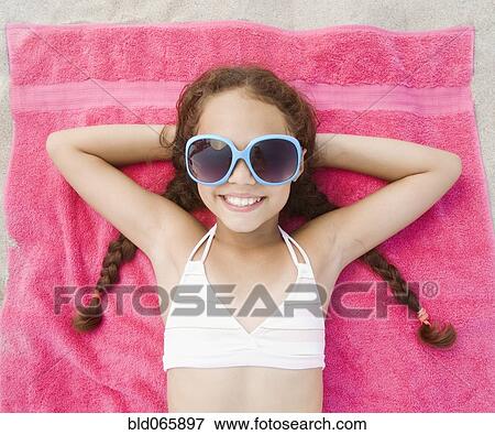Stock Photo - Hispanic girl laying on beach in bikini and sunglasses. Fotosearch