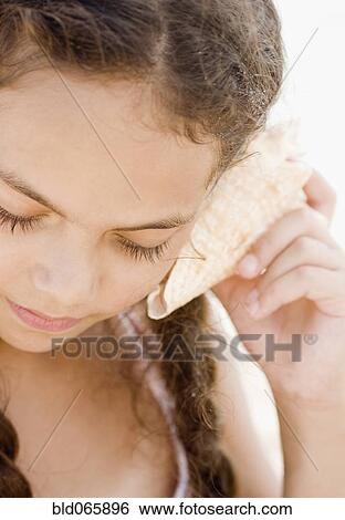 Stock Photograph - Hispanic girl listening to seashell. Fotosearch