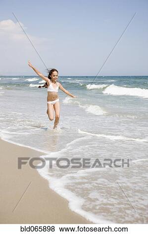 Stock Photo - Hispanic girl running in waves at beach. Fotosearch