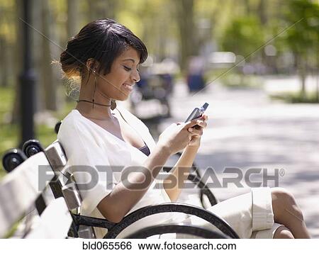 Hispanic woman text messaging on cell phone in park View Large Photo Image Stock Photograph - Hispanic woman text messaging on cell phone in park. Fotosearch