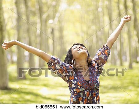 Stock Image - Hispanic woman with arms outstretched in park. Fotosearch