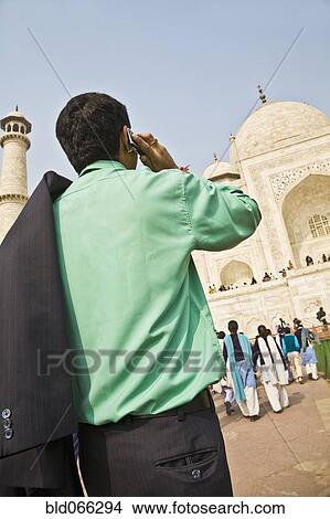 Picture - Indian businessman on cell phone visiting Taj Mahal. Fotosearch