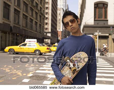 Stock Photography - Indian man on city street holding skateboard. Fotosearch