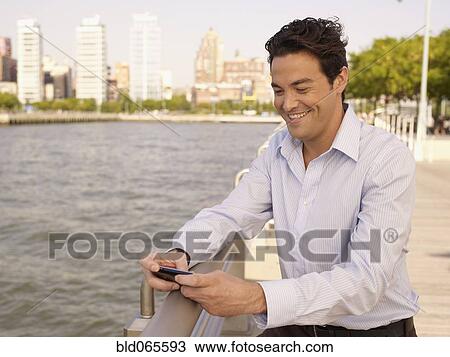 Stock Image - Man at waterfront text messaging on cell phone. Fotosearch