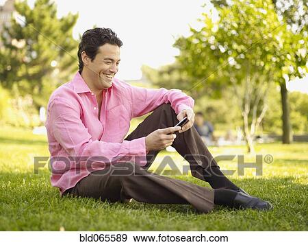 Man sitting in grass text messaging in park View Large Photo Image Stock Photo - Man sitting in grass text messaging in park. Fotosearch