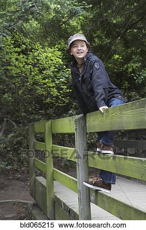 Stock Photography - Mixed race boy climbing on wooden fence. Fotosearch