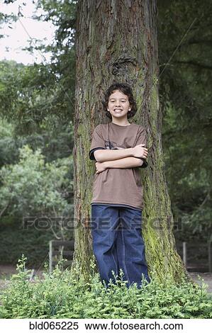 Stock Photography - Mixed race boy posing next to tree trunk. Fotosearch
