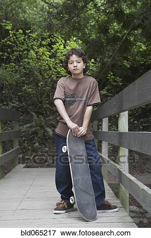 Stock Photo - Mixed race boy standing with skateboard. Fotosearch