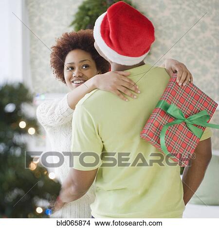 Mixed race woman hugging boyfriend and holding Christmas present View Large Photo Image Picture - Mixed race woman hugging boyfriend and holding Christmas present. Fotosearch