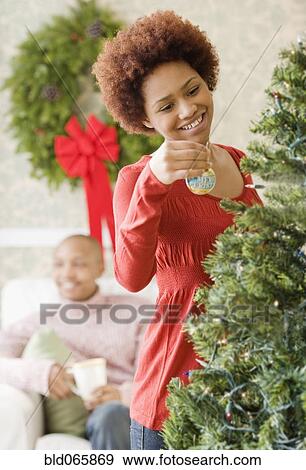Stock Photo - Mixed race woman placing ornament on Christmas tree. Fotosearch