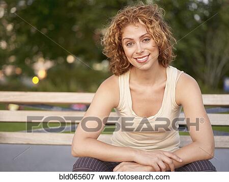 Stock Photo - Mixed race woman sitting on bench in park. Fotosearch