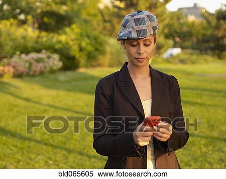 Stock Photography - Mixed race woman text messaging on cell phone in park. Fotosearch