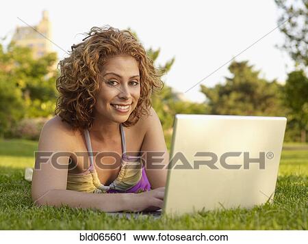 Stock Image - Mixed race woman typing on laptop in park. Fotosearch