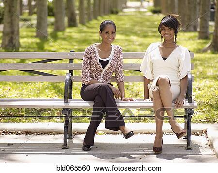 Stock Image - Women in trendy fashions sitting in park. Fotosearch