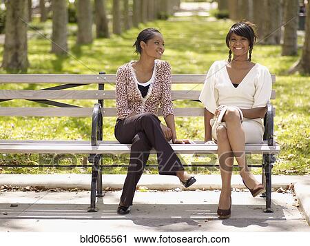 Stock Image - Women in trendy fashions sitting in park. Fotosearch