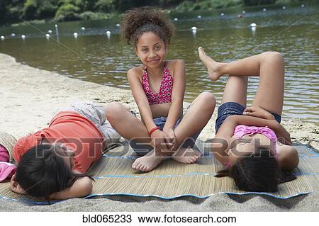 Stock Image - Young girl friends relaxing near lake. Fotosearch