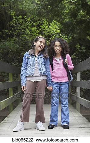 Stock Image - Young school girls posing on wooden bridge. Fotosearch