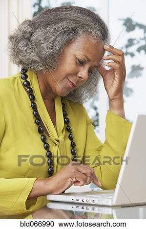 Stock Image - African woman using laptop at home. Fotosearch