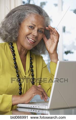 Stock Image - African woman using laptop at home. Fotosearch