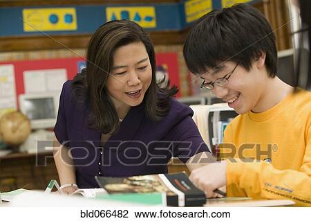 Stock Image - Asian school teacher helping student. Fotosearch