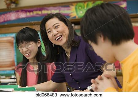Stock Image - Asian school teacher laughing with students. Fotosearch