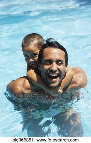 Stock Image - Father giving son piggyback ride in swimming pool. Fotosearch