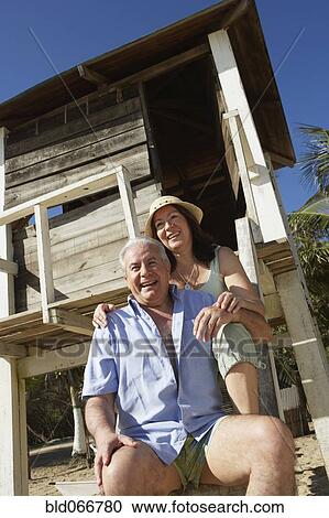 Stock Image - Hispanic couple sitting near lifeguard tower. Fotosearch
