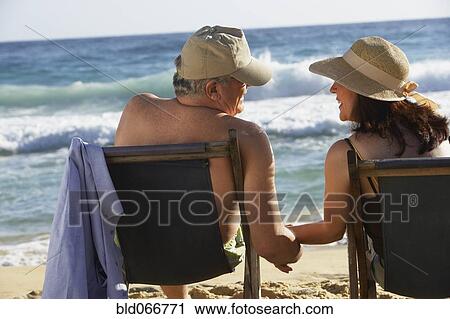 Stock Image - Hispanic couple sitting on beach. Fotosearch