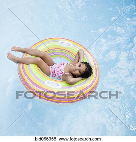 Stock Photo - Hispanic girl floating in pool in inflatable ring. Fotosearch