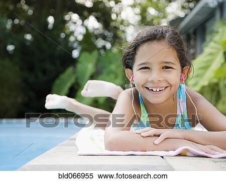 Stock Photography - Hispanic girl listening to music at poolside. Fotosearch