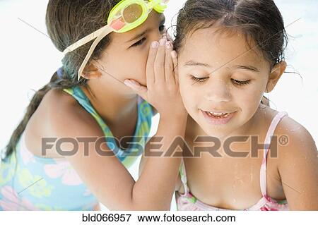 Stock Photo - Hispanic girl whispering to sister. Fotosearch
